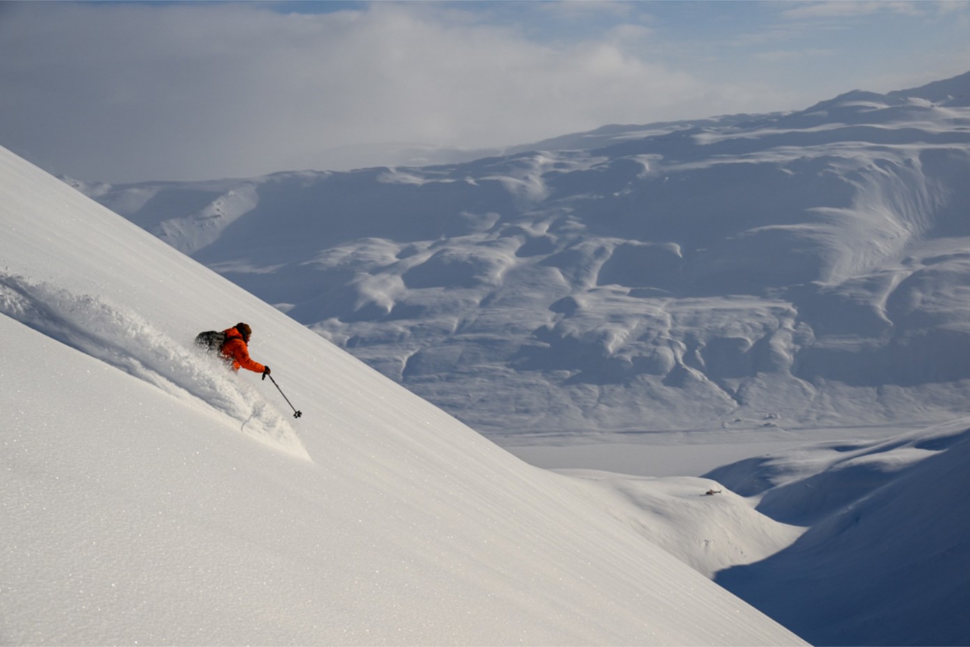 A skier in a snow cloud going downhill in an Icelandic mountain range.